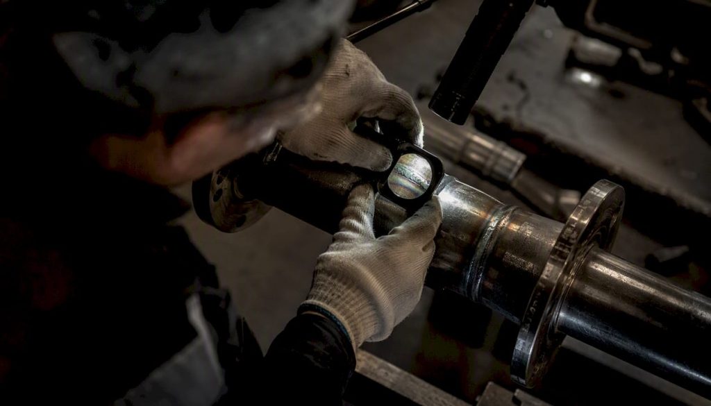 Hands inspecting weld seam with magnifier and light